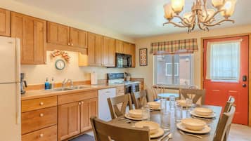 A kitchen with wooden cabinets, a refrigerator, a microwave, and a dining table set for four.