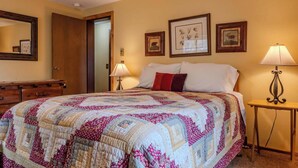 Une chambre à coucher avec un grand lit, une commode, une table de chevet avec une lampe et des tableaux encadrés au mur.