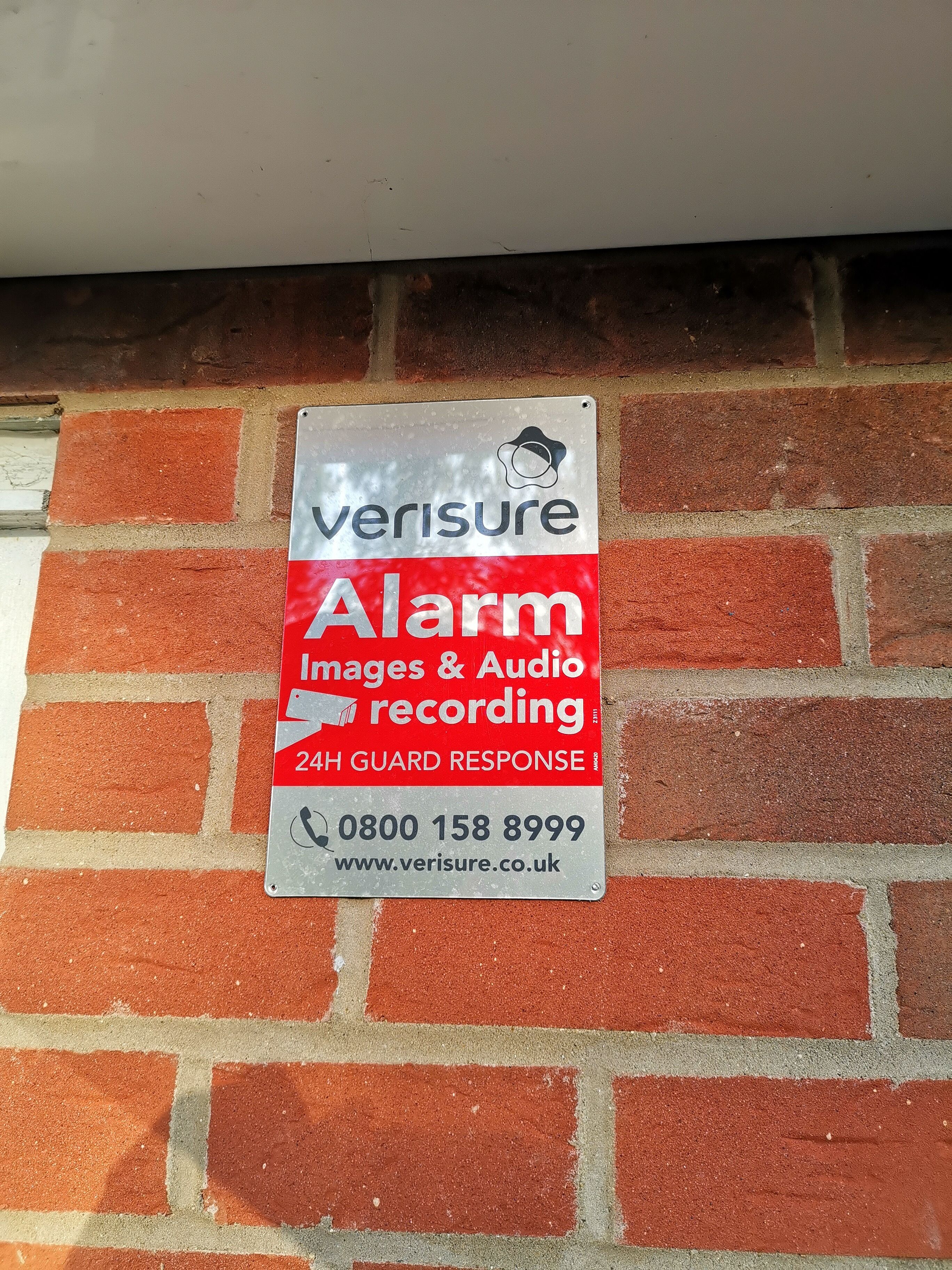 A security alarm sign on a brick wall.