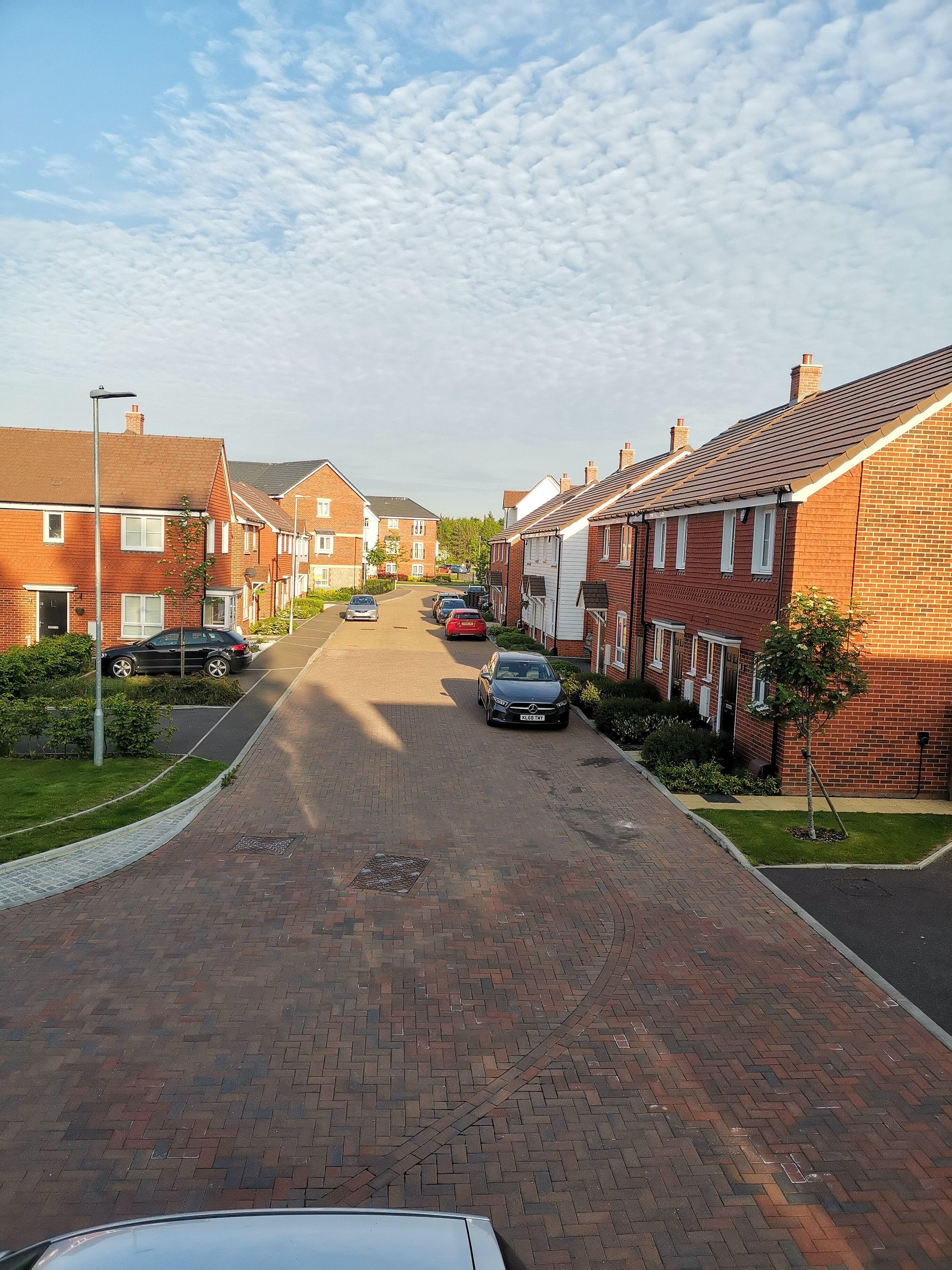Calle residencial bordeada de casas de ladrillo, con una vía pavimentada y automóviles estacionados.