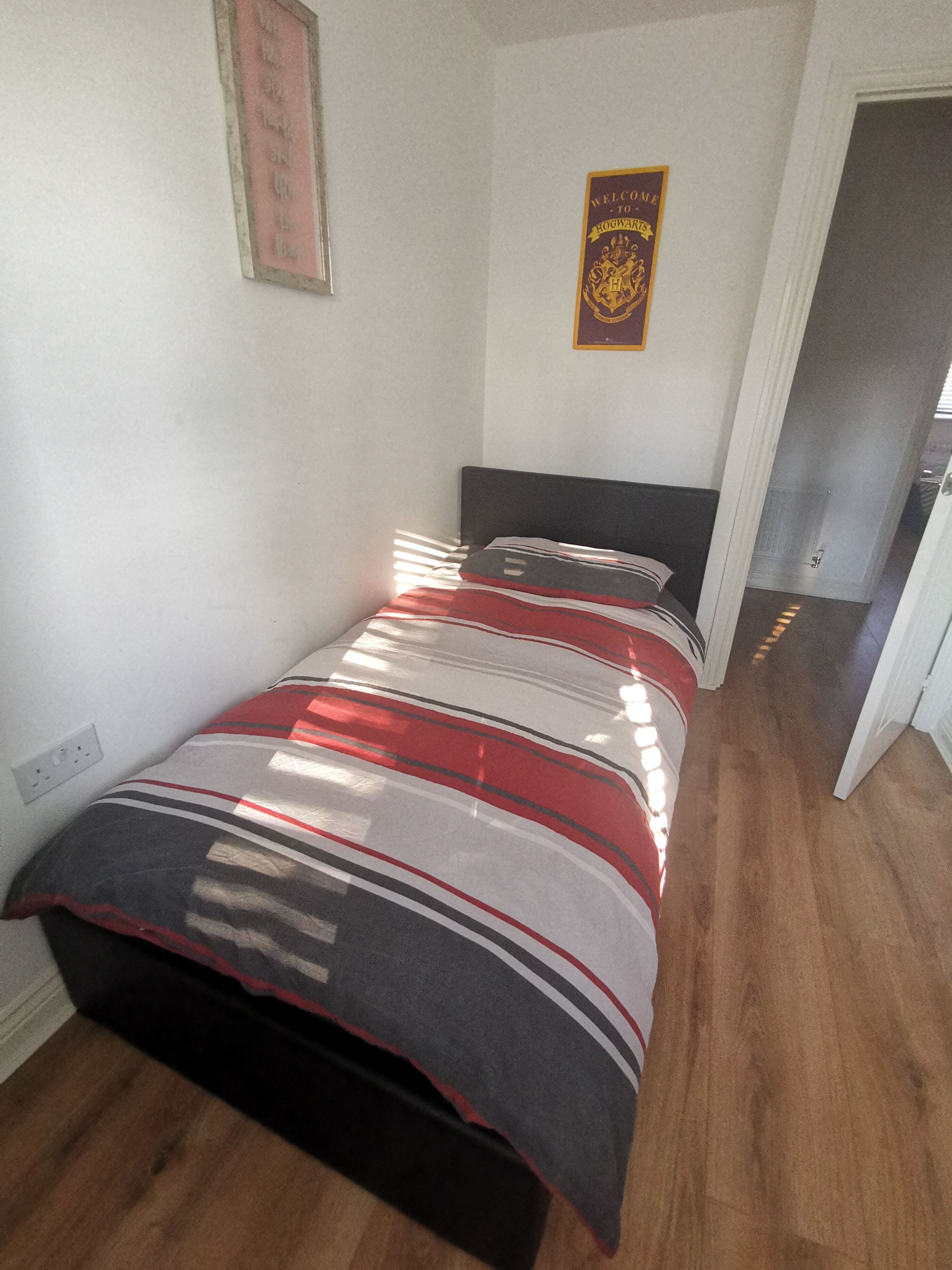 Ein Schlafzimmer mit einem Bett, einem gerahmten Willkommensschild und einer Tür zu einem anderen Raum.