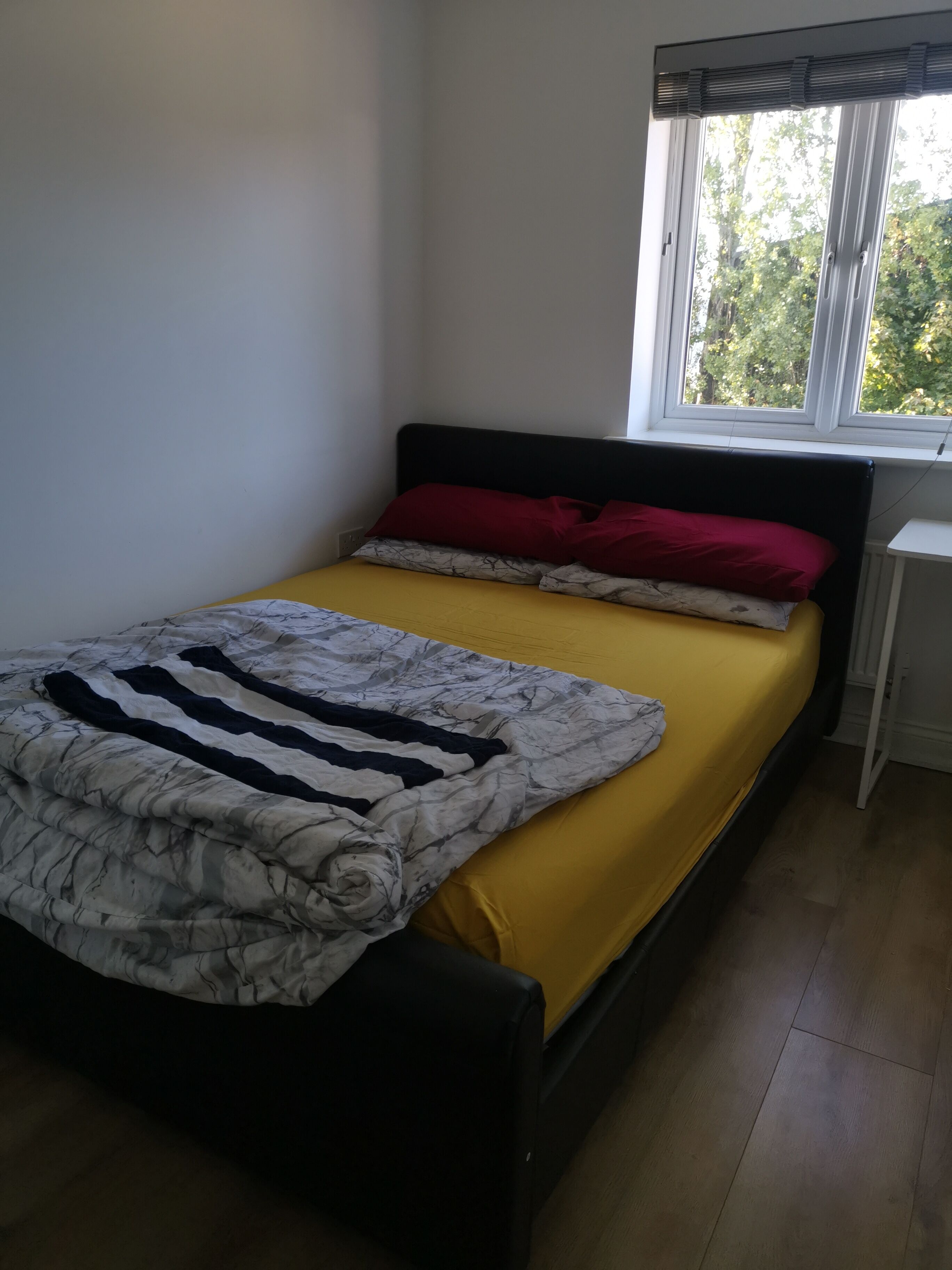 Ein Bett mit einem gelben Matratze, einem schwarzen Kopfteil und einer gemusterten Decke.