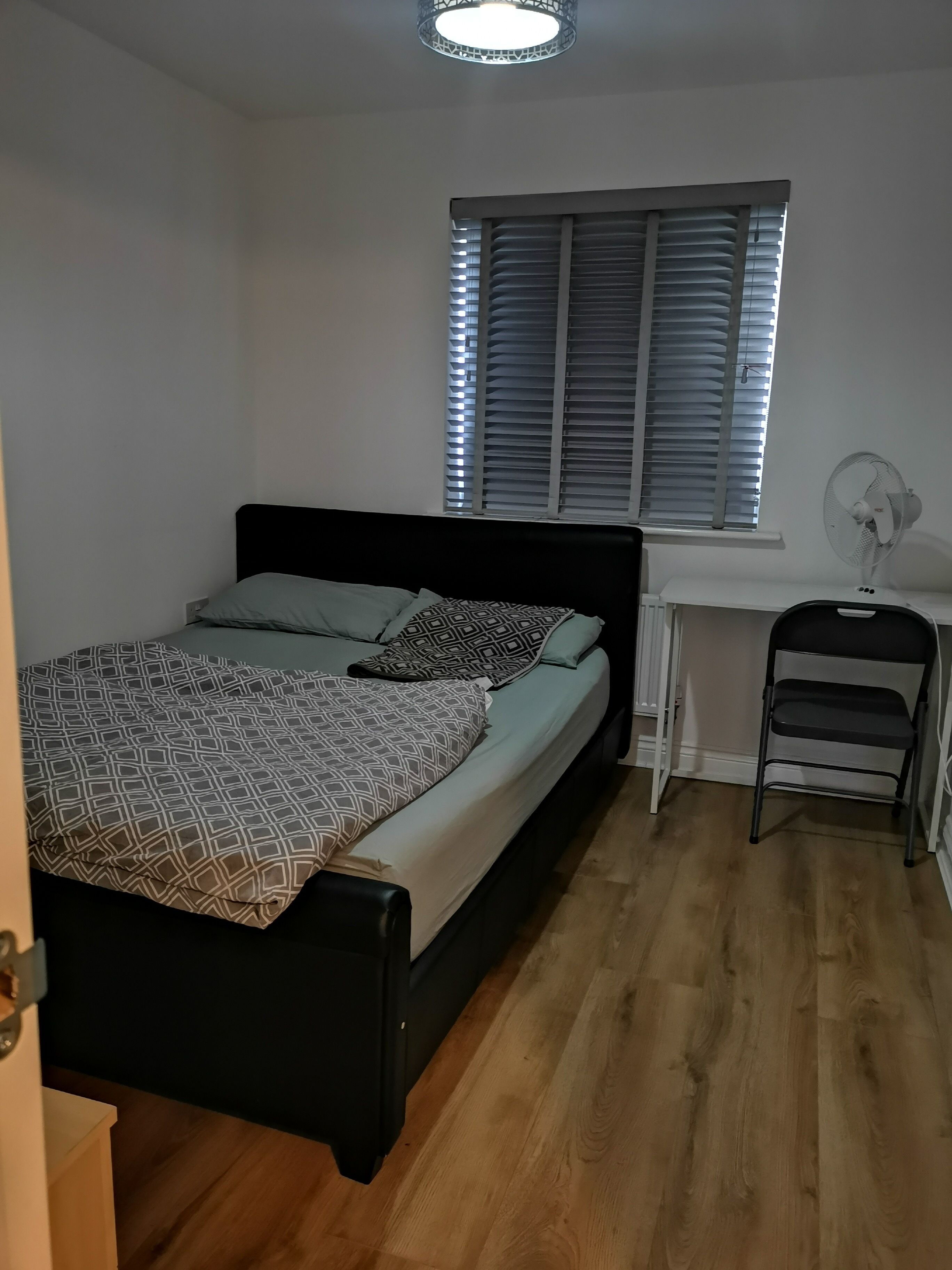 A bedroom with a bed, a desk, a chair, and a window with blinds.