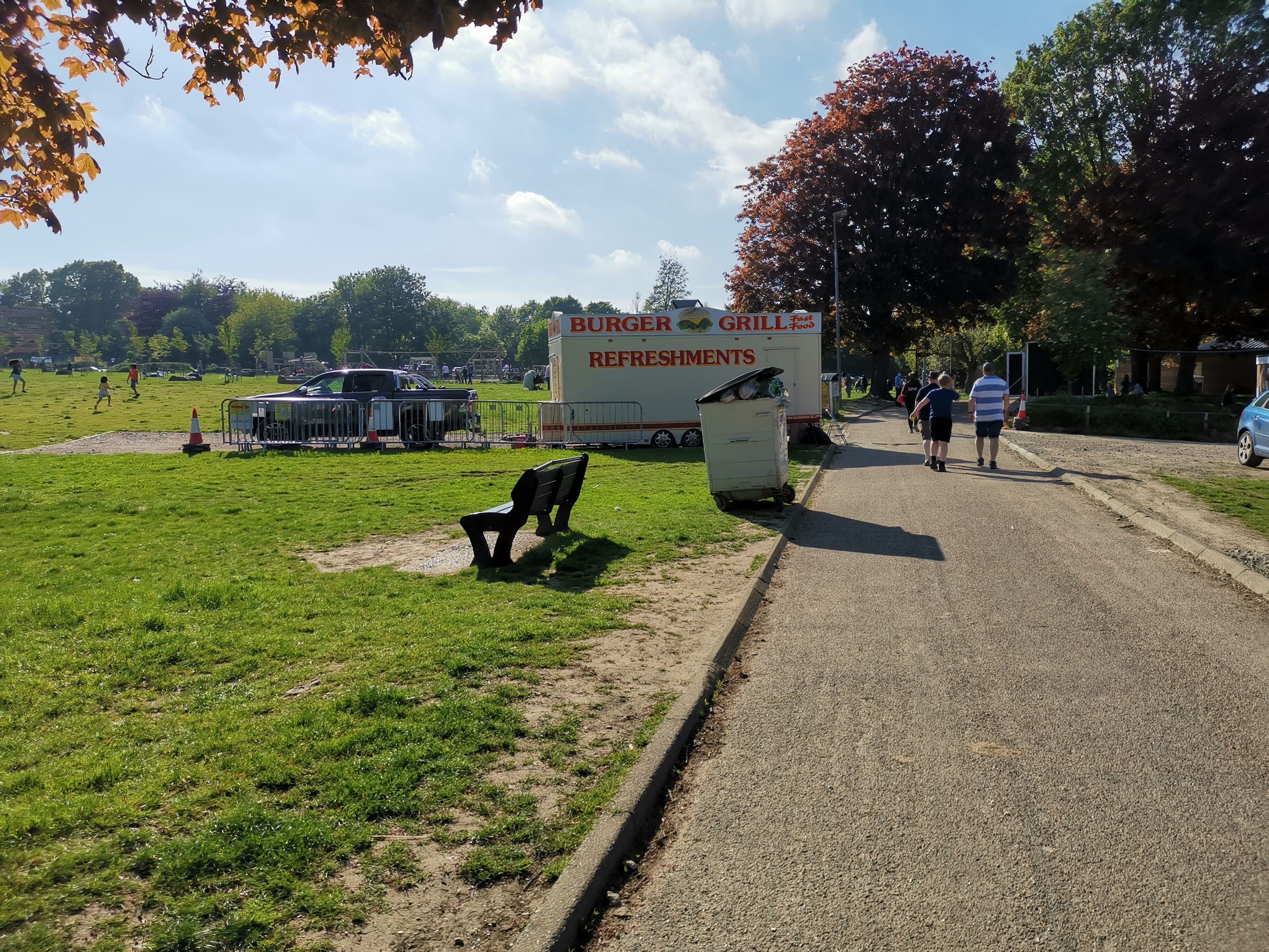 A grassy area with a bench, a road, and a Burger Grill Refreshments truck.