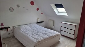 Ein Schlafzimmer mit Bett, Schreibtisch, Heizkörper, Regal und Dachfenster.