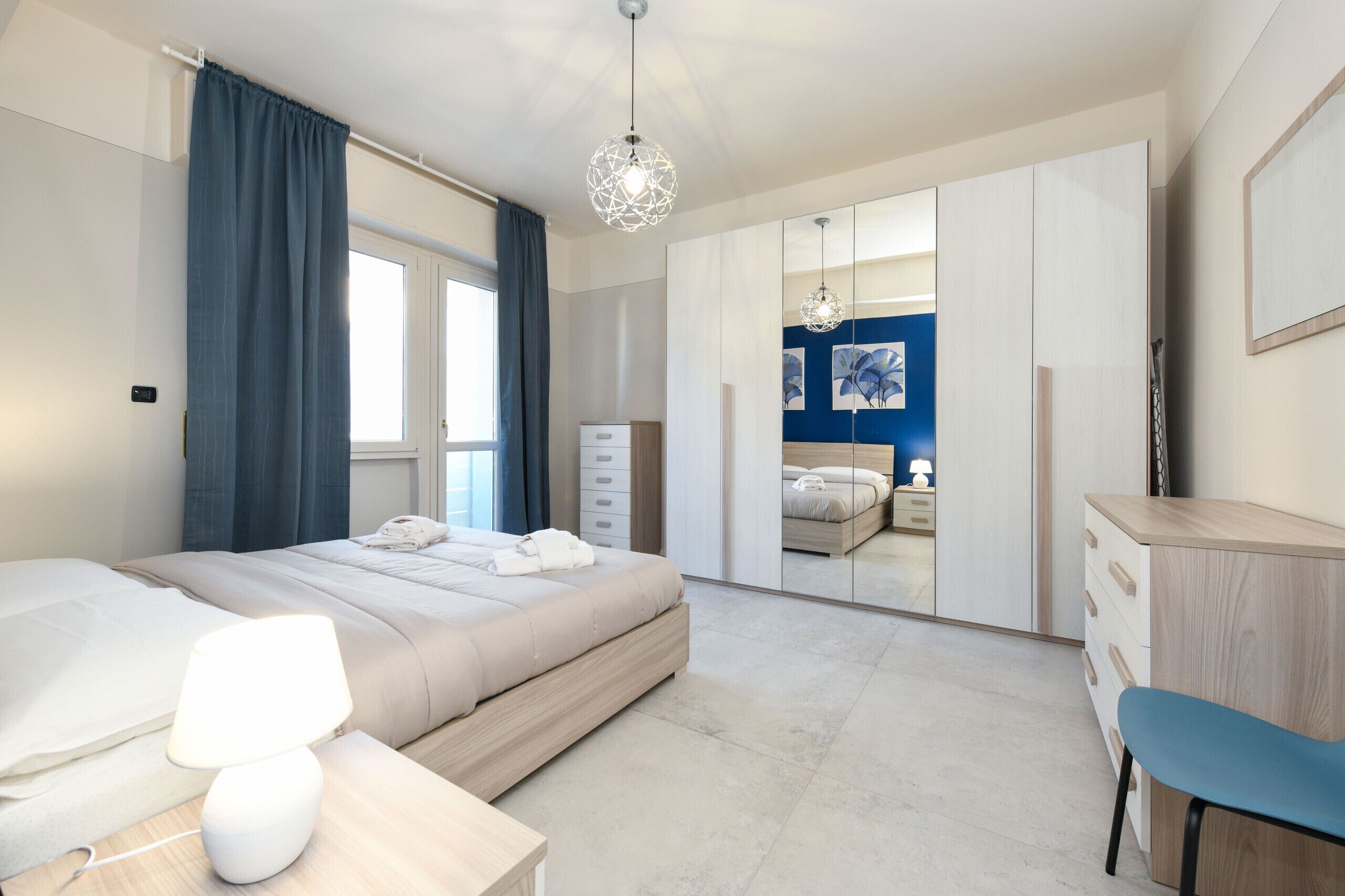 A modern bedroom with a bed, bedside table, lamp, wardrobe, and a desk with a chair.