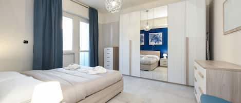 Et moderne soveværelse med seng, sengebord, lampe, garderobeskab og et skrivebord med stol.