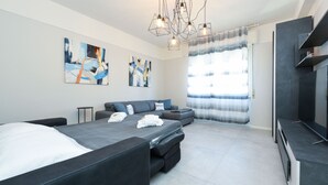 Ein modernes Schlafzimmer mit einem großen Bett, einer Schlafcouch, einem Fernseher und abstrakter Kunst an den Wänden.