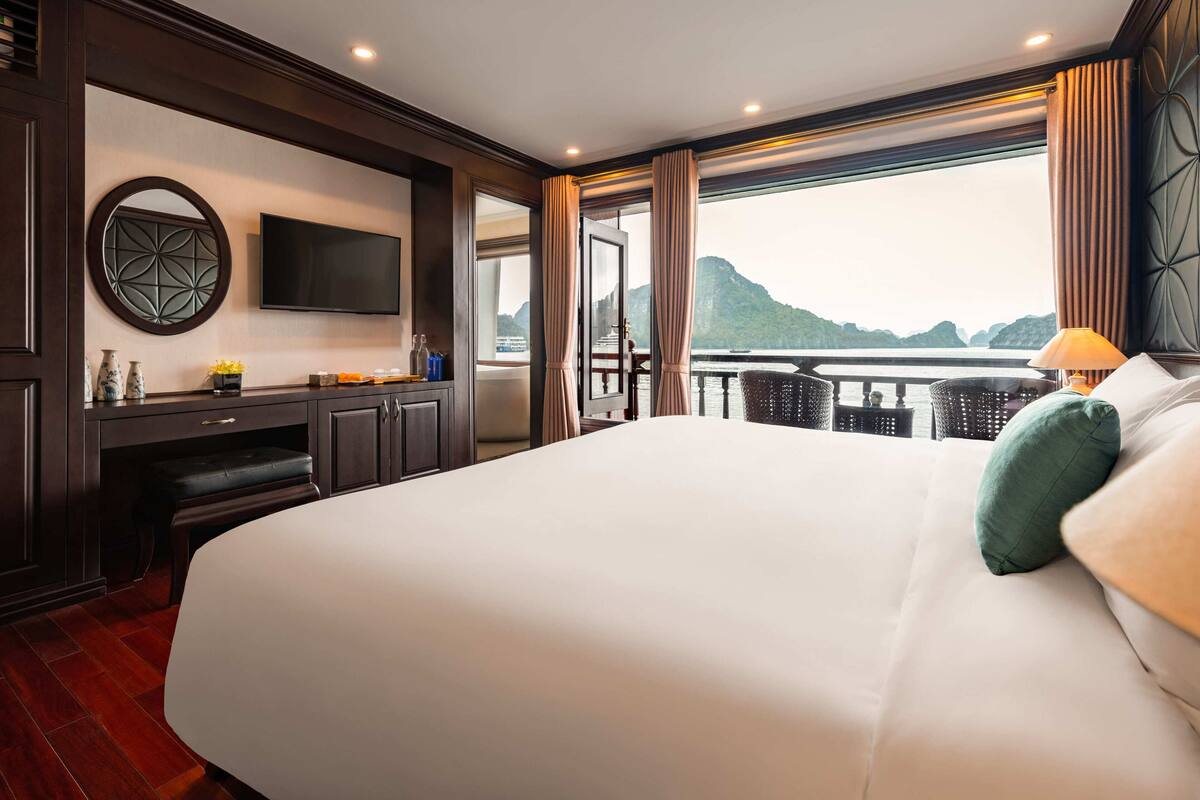 A spacious bedroom with a large bed, a desk, a television, and a view of a body of water.
