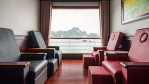 A balcony with seating, a view of the water, and a painting on the wall. - Aqua Of The Seas Cruise Ha Long (Tuan Chau)