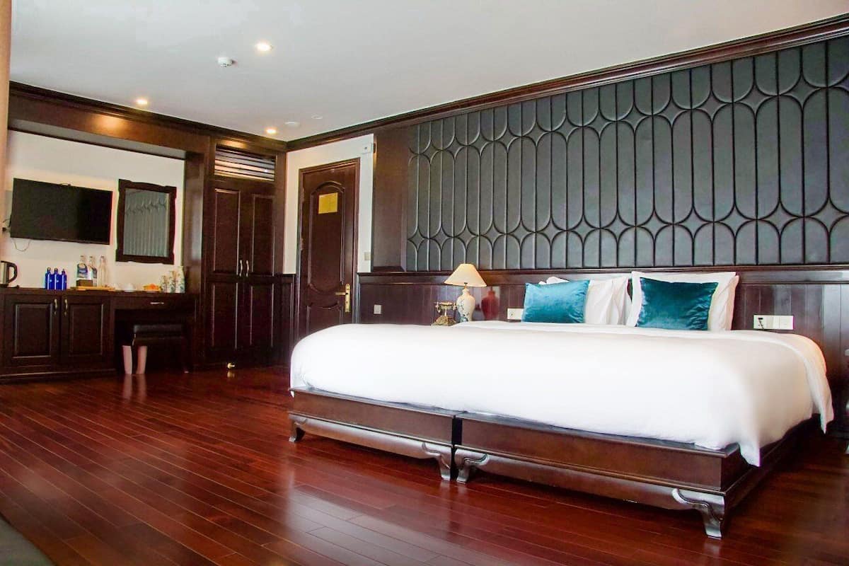 A spacious hotel room with a large bed, a wooden dresser, a vanity with a mirror, and a television on the wall.