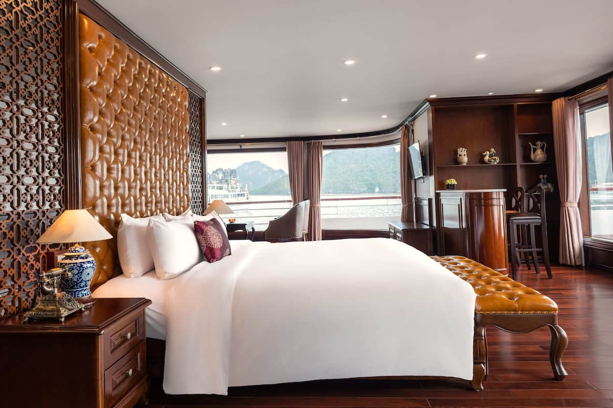 A luxurious bedroom with a large bed, a wooden bench, and a view of a body of water.