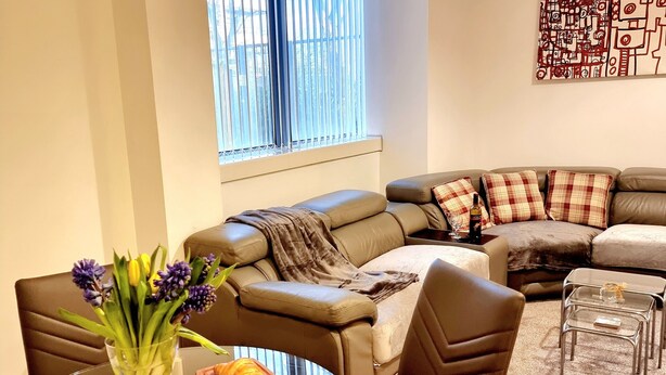 Ett modernt vardagsrum med en brun lädersoffa, ett soffbord i glas och en matplats med en vas av glas fylld med blommor.