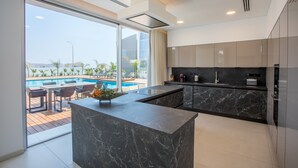 Een moderne keuken met een marmeren aanrechtblad, uitzicht op een zwembad en een eethoek met terrasmeubels.