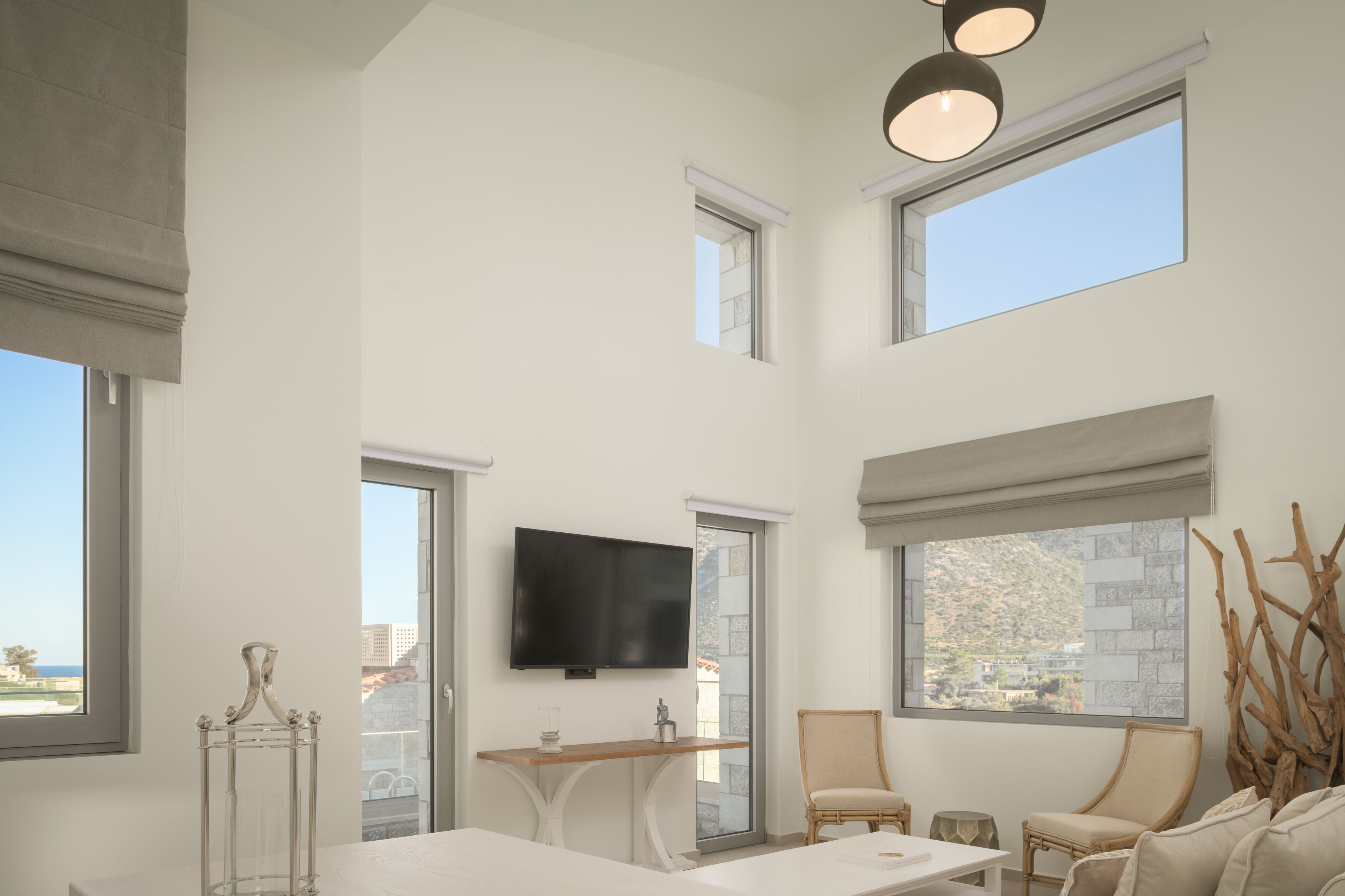 A spacious living room with a flat-screen TV, large windows, and a balcony view.
