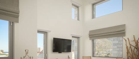 A spacious living room with a flat-screen TV, large windows, and a balcony view.