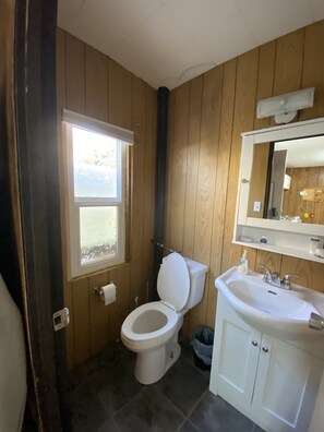Kylpyhuone, jonka seinät ovat puuta, ja jossa on valkoinen wc-istuin, pesuallas ja ikkuna.