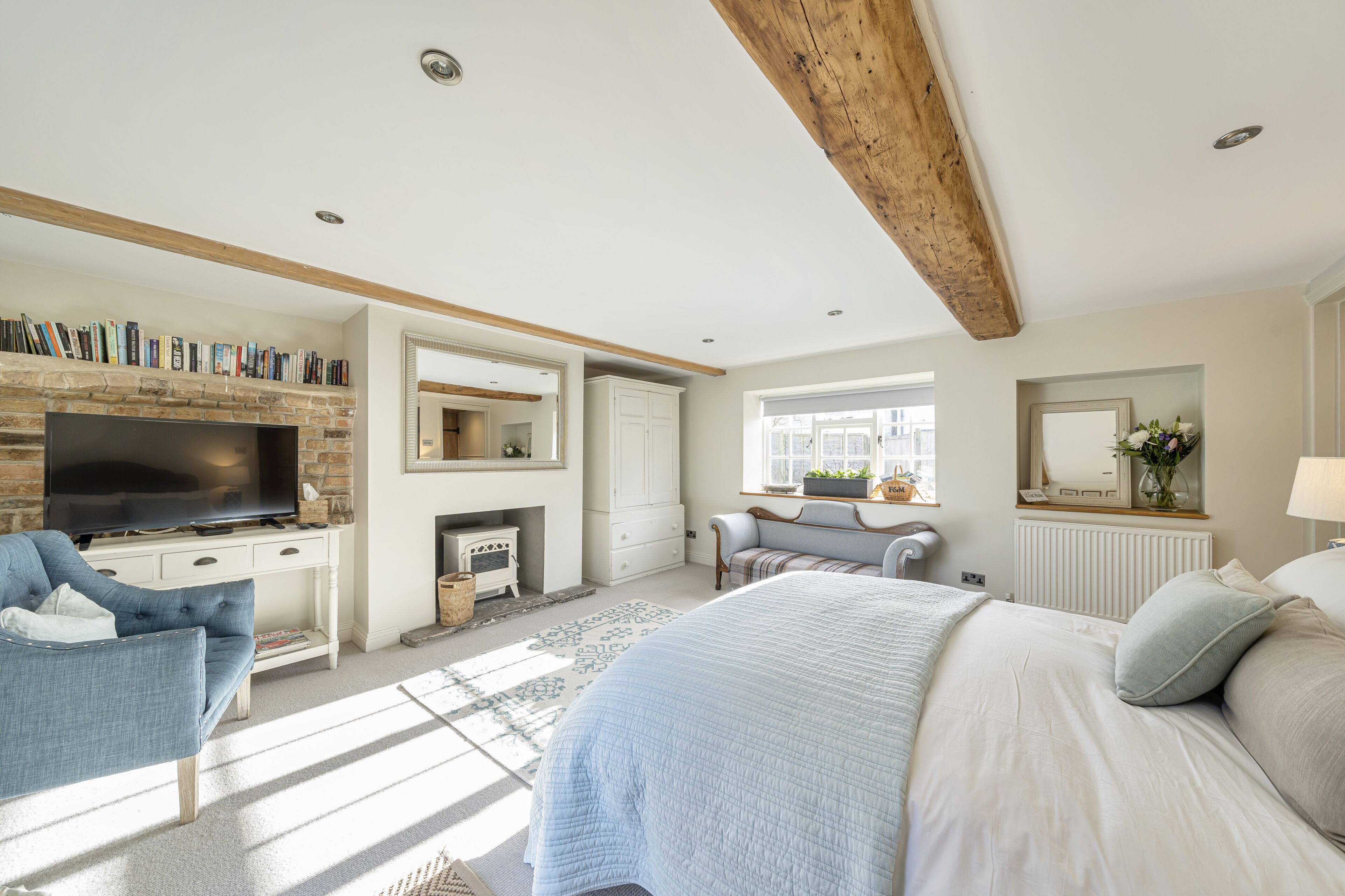 A bedroom with a large bed, a TV, a fireplace, and a bookshelf.