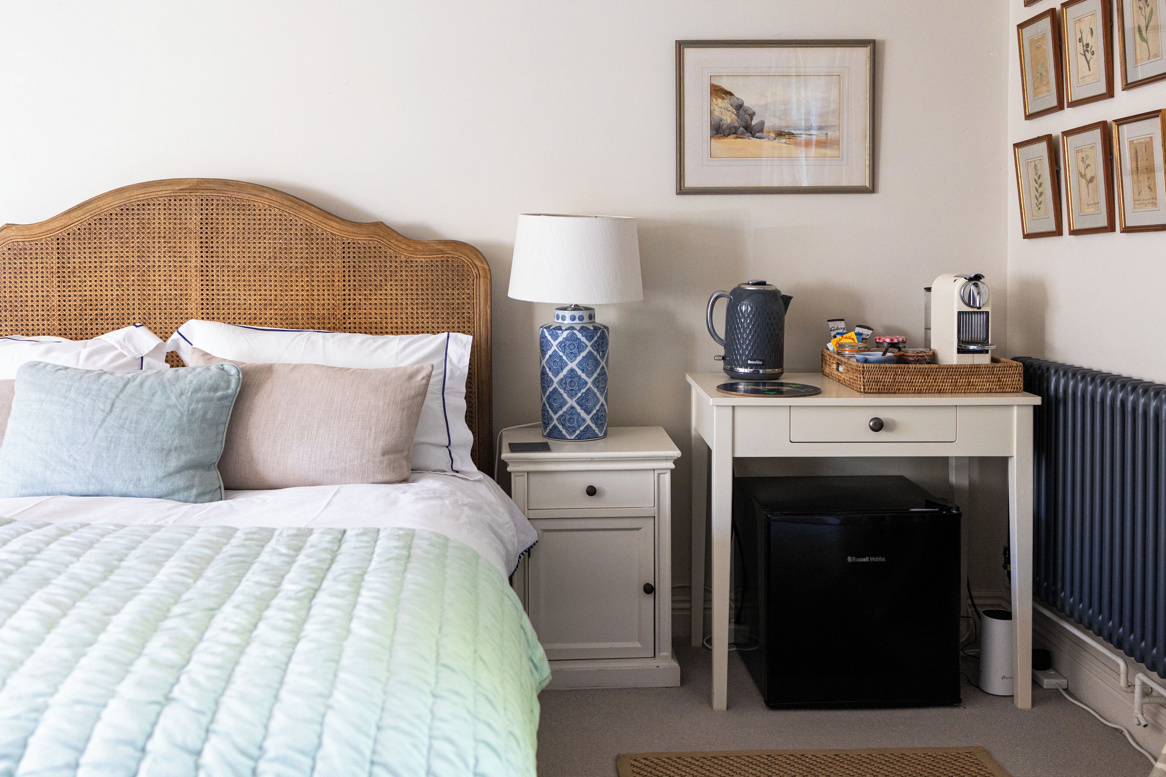 A neatly arranged hotel room with a bed, bedside table, lamp, coffee maker, and a small refrigerator.