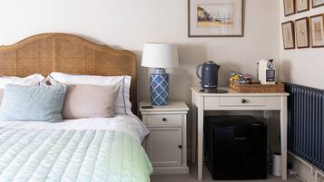 A neatly arranged hotel room with a bed, bedside table, lamp, coffee maker, and a small refrigerator.
