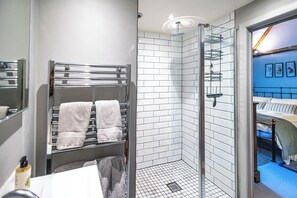 A modern bathroom with a glass shower enclosure, a towel rack with multiple towels, and a visible bathroom sink. - Barton Cottage Bed and Breakfast (Dorchester)