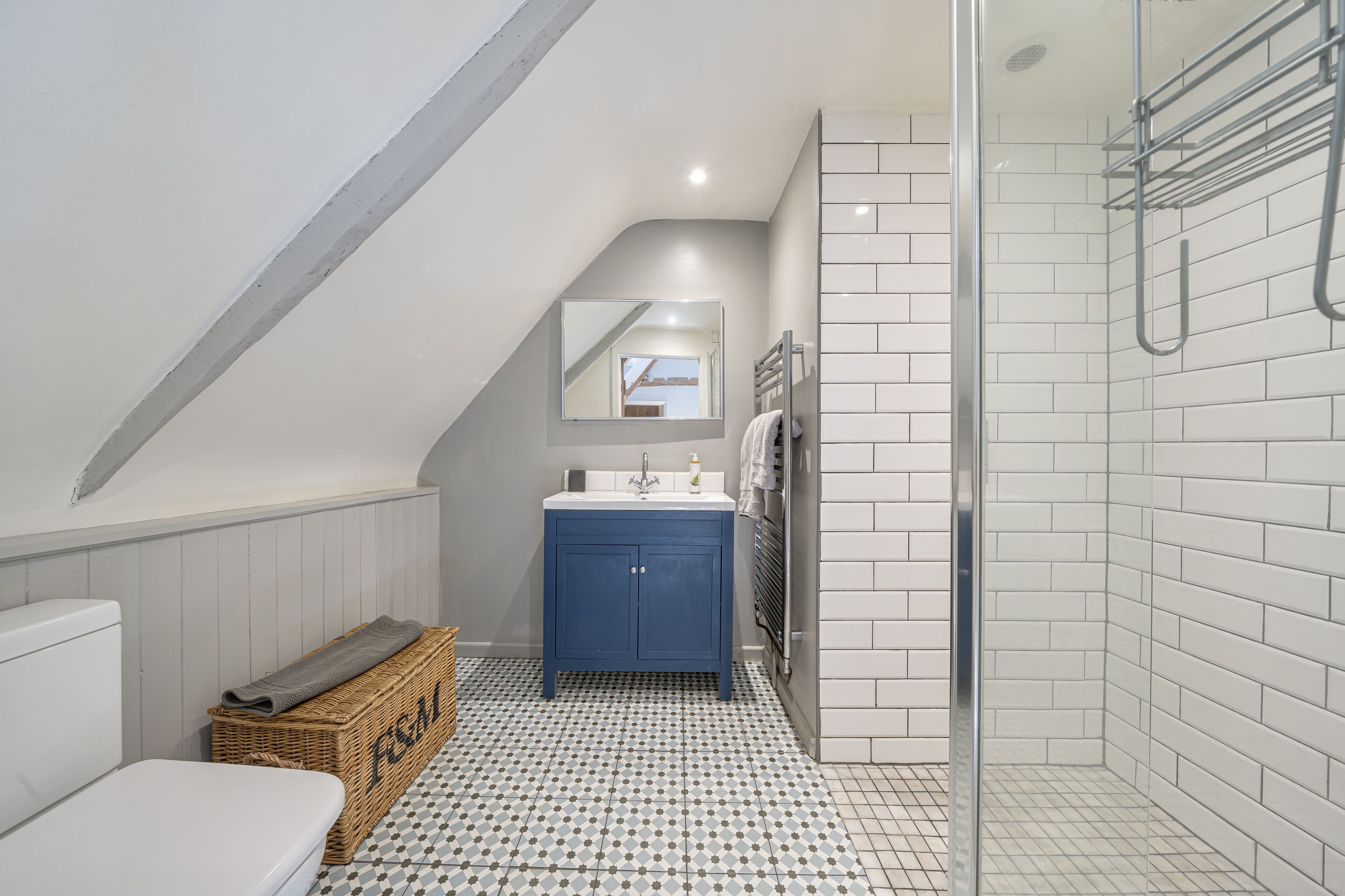 A bathroom with a white toilet, a blue vanity, a glass shower enclosure, and a patterned floor.