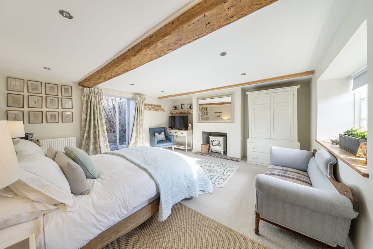 A bedroom with a large bed, a chair, a desk, a fireplace, and a wardrobe.