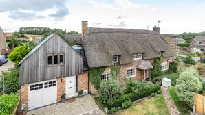 A traditional thatched-roof house with a wooden extension, surrounded by a well-maintained garden and neighboring houses. - Barton Cottage Bed and Breakfast (Dorchester)