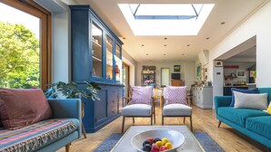 A spacious living room with a large window, a blue cabinet, a teal sofa, and a dining area with chairs and a table. - Barton Cottage Bed and Breakfast (Dorchester)