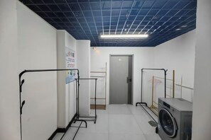 A laundry room with a washing machine, a drying rack, and a door leading to another room. - Loft Hotel (Changyi)