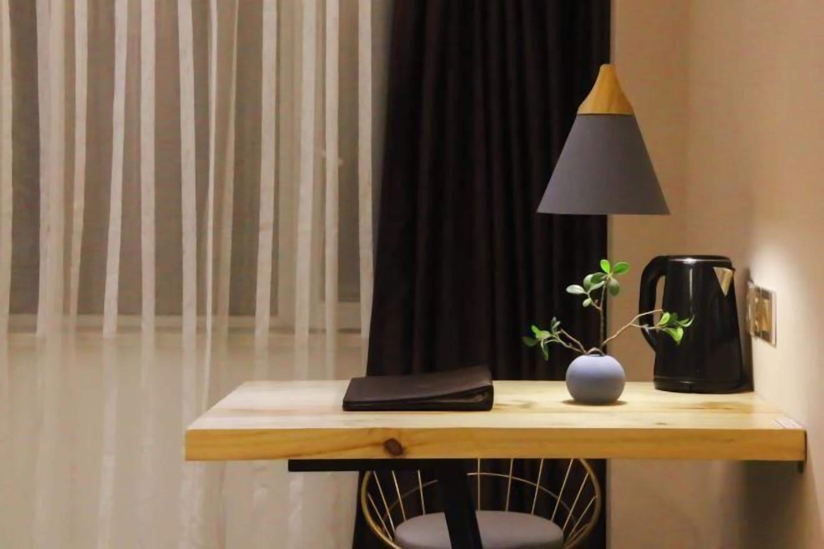 Una pequeña mesa de madera con una lámpara negra, un florero con una planta y una cafetera.