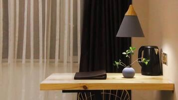 Una pequeña mesa de madera con una lámpara negra, un florero con una planta y una cafetera.