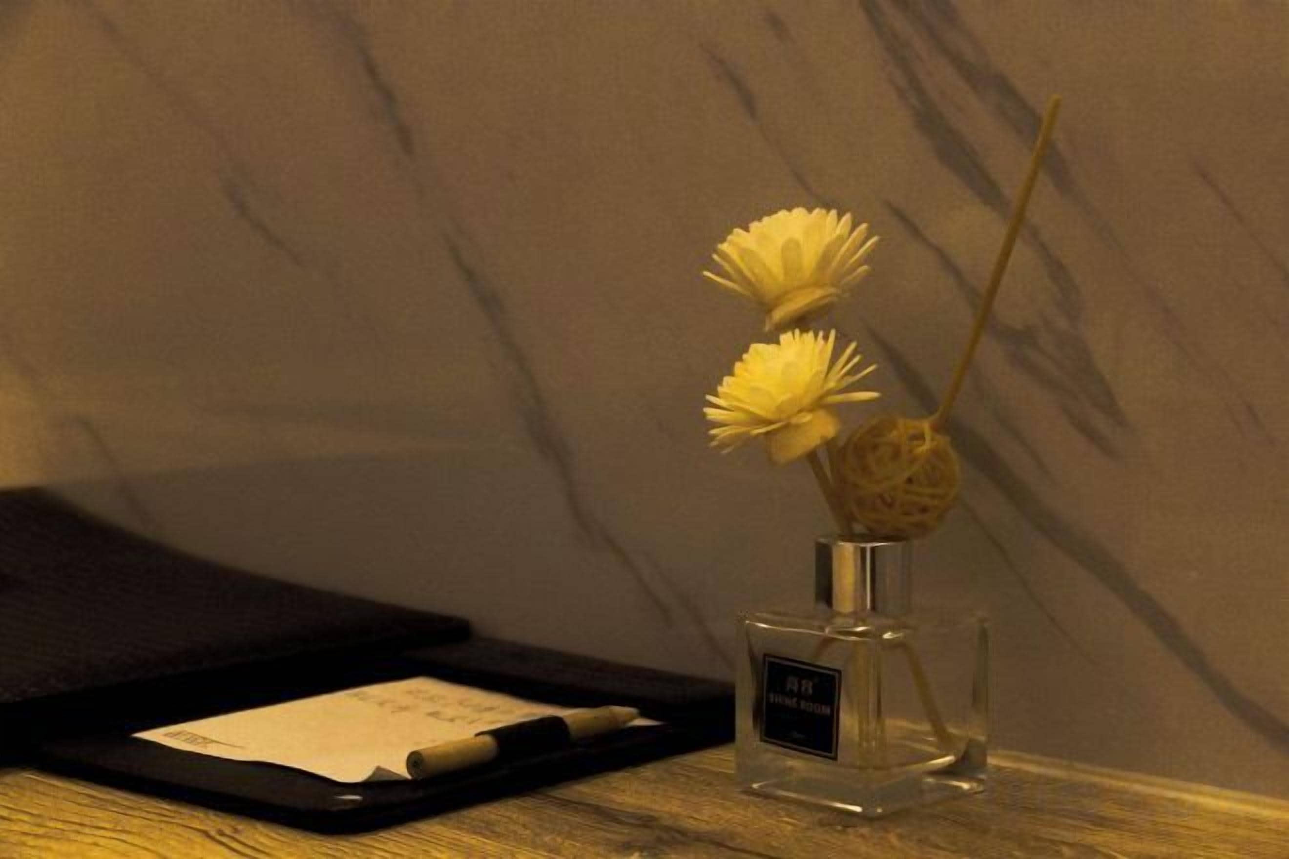 Una tableta sobre una superficie de madera, con un frasco de perfume y un jarrón lleno de flores.