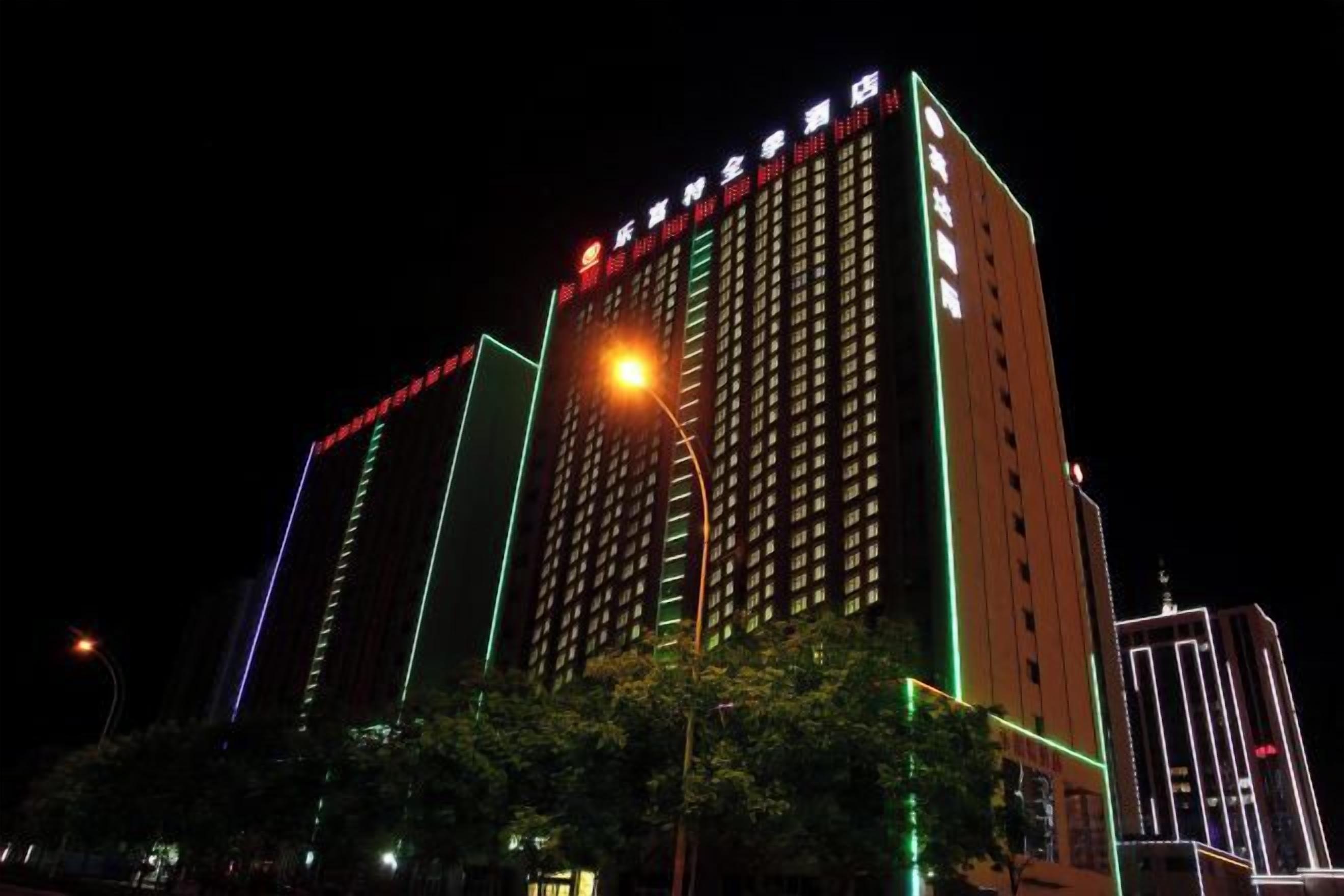 A high-rise hotel with multiple floors, illuminated by external lighting, and surrounded by trees.