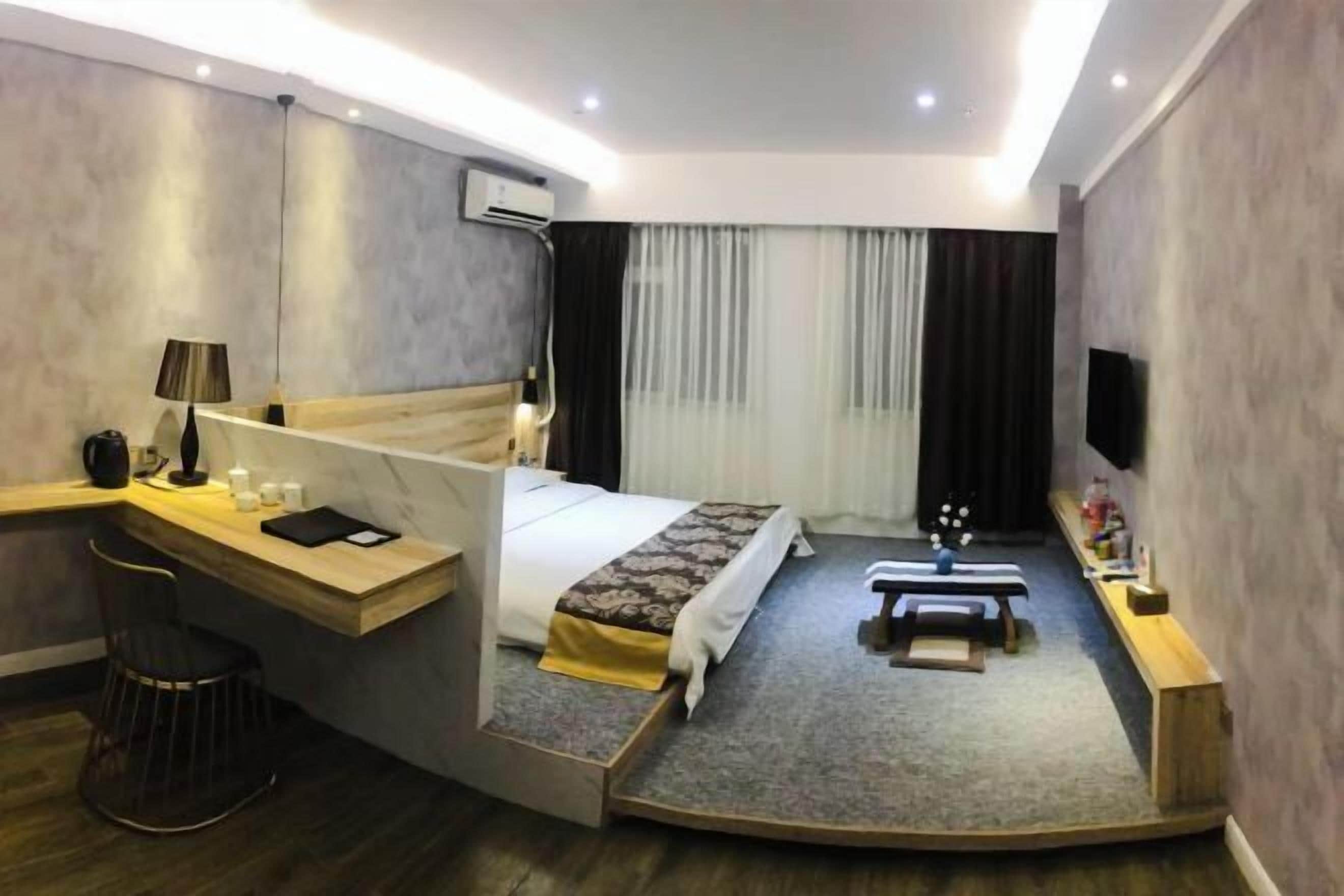 Una habitación de hotel moderna con una cama curvada, un escritorio, un banco y un televisor.