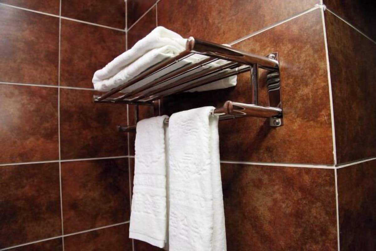 A bathroom with a towel rack holding two white towels and a metal shelf with additional towels.