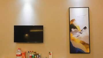 Ein Flachbildfernseher ist an einer Wand über einem Regal montiert, auf dem eine Wasserflasche, Dosen und eine kleine Schachtel stehen.
