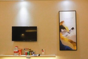 Un televisor de pantalla plana montado en una pared sobre una repisa con varios objetos, incluyendo una botella de agua, latas y una caja pequeña.