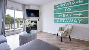 A living room with a TV, a fireplace, a striped armchair, and a wall sign reading "RIVER TO BAY GETAWAY". - Beach1 Waterfront Stunning Views (Wasaga Beach)