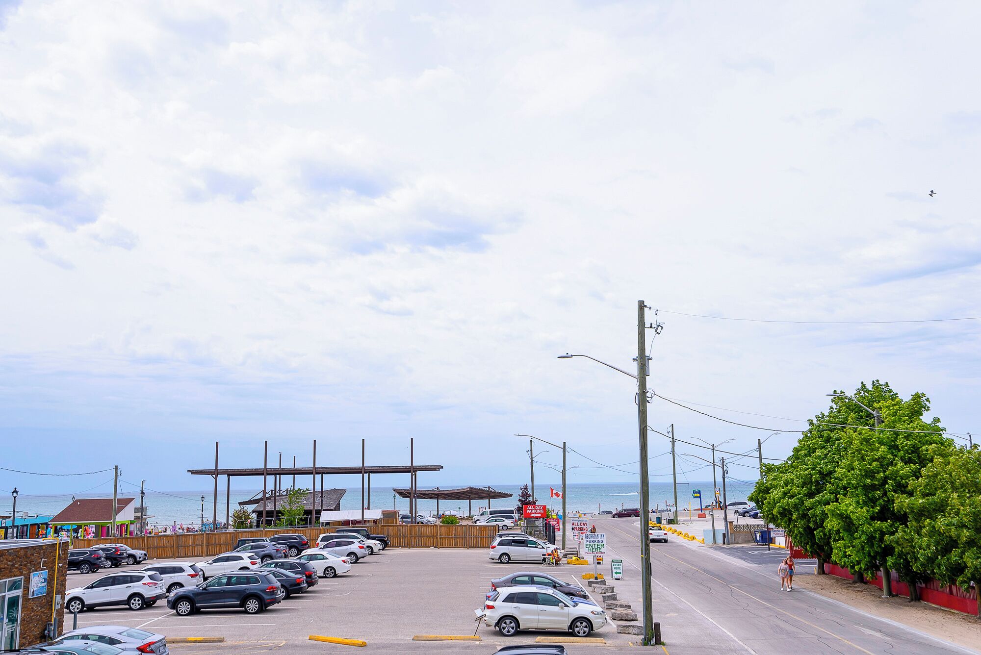 Ein Parkplatz mit Autos, im Hintergrund ein Strand und eine Holzkonstruktion.
