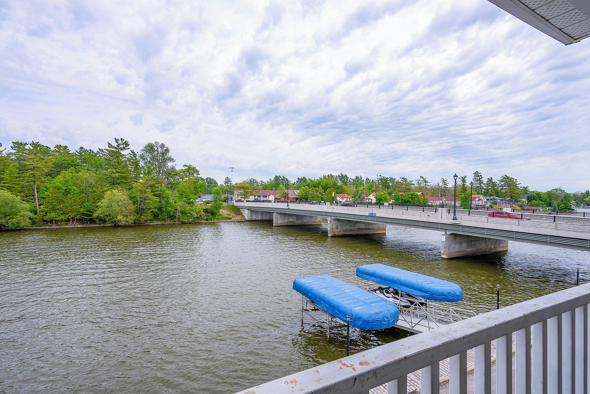 Un río con un puente, un muelle con toldos azules y una barandilla blanca.