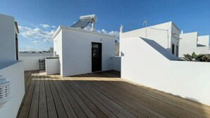 Una terrazza sul tetto con un pavimento in legno, un piccolo edificio bianco con una porta nera e un'antenna parabolica.