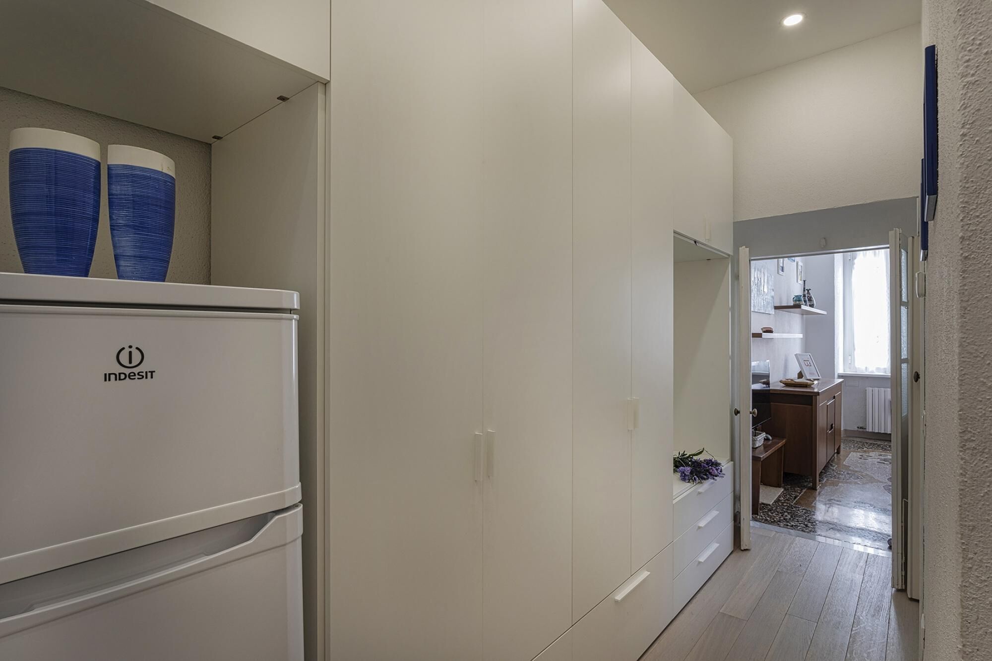 Un pasillo con un refrigerador blanco, un armario blanco y un mueble de madera.