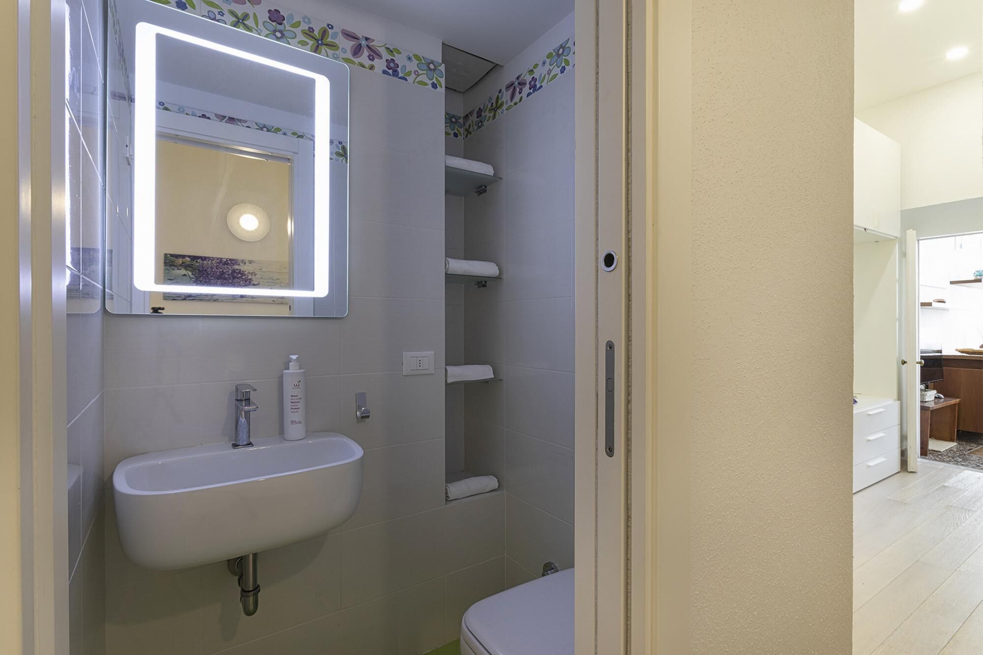 Un baño con lavamanos blanco, un espejo con iluminación integrada, ducha e inodoro.