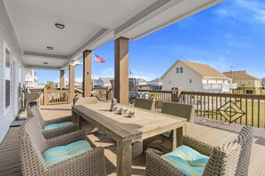 A covered outdoor patio with wicker furniture and a wooden table, featuring a view of houses and a clear sky. - Surf & Seahorse 4 Bedroom Home by RedAwning (Port Bolivar)