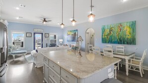 A spacious kitchen with a central island, pendant lights, and a dining area with white chairs.