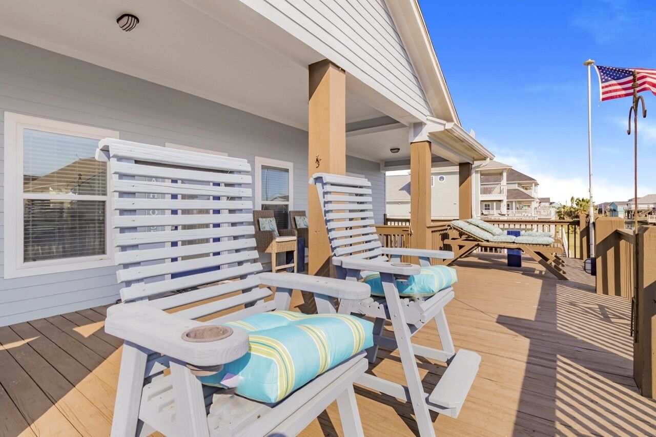 A covered outdoor area with white lounge chairs and a wooden deck.