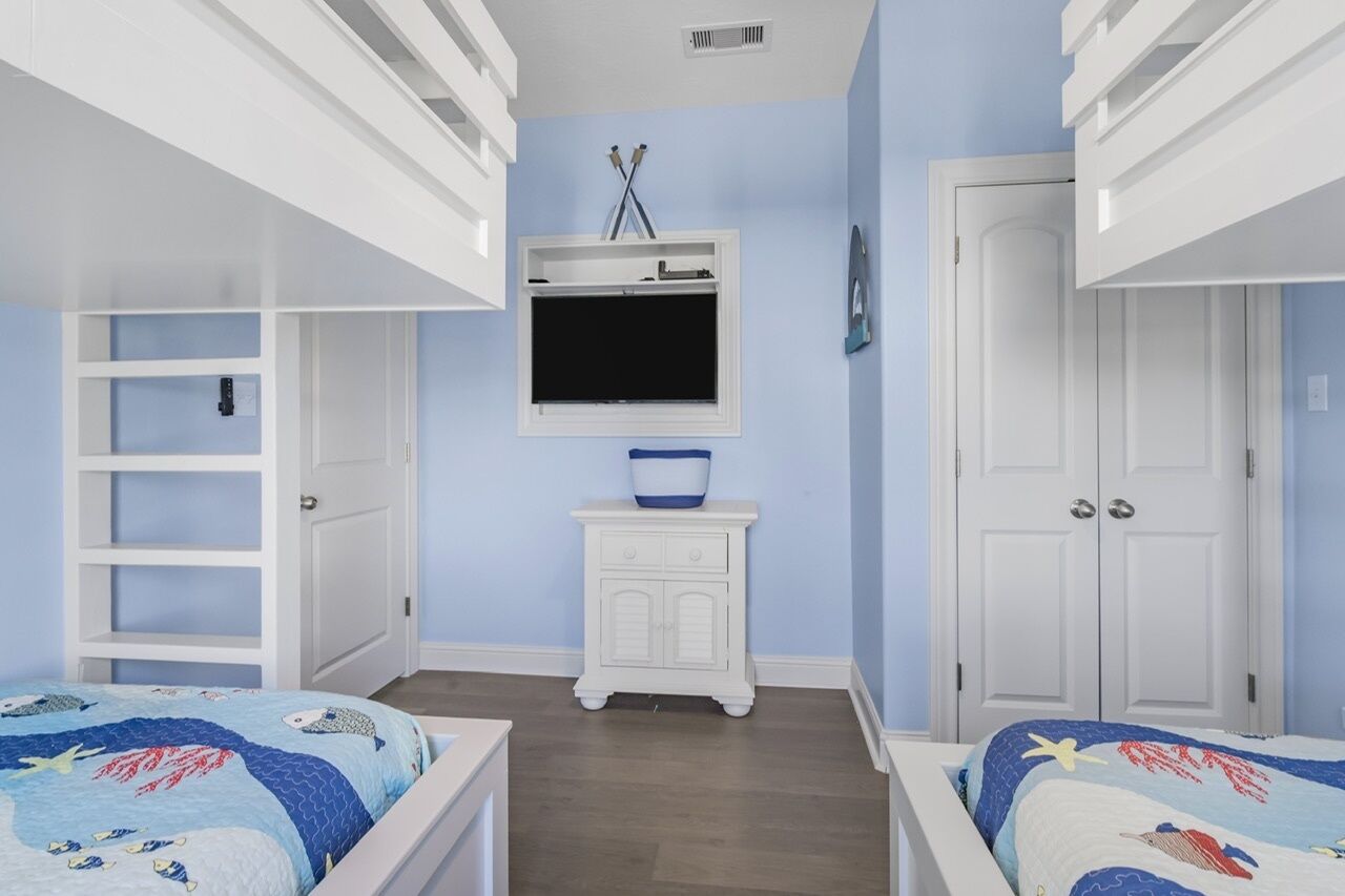 A bedroom with bunk beds, a TV, a small cabinet, and a door.