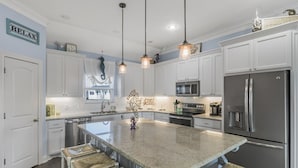 A spacious kitchen with white cabinets, a large island with bar stools, stainless steel appliances, and pendant lighting.
