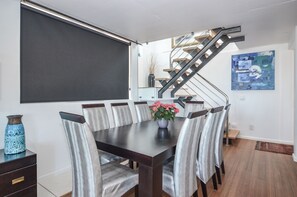 A dining area with a dark wooden table, six chairs, and a vase with flowers. A staircase with a metal railing is visible in the background.